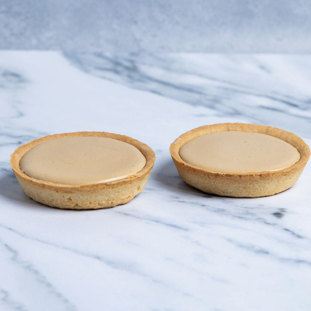 Two small pastry tarts with a creamy filling on a marble surface