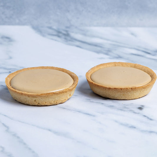 Two small pastry tarts with a creamy filling on a marble surface