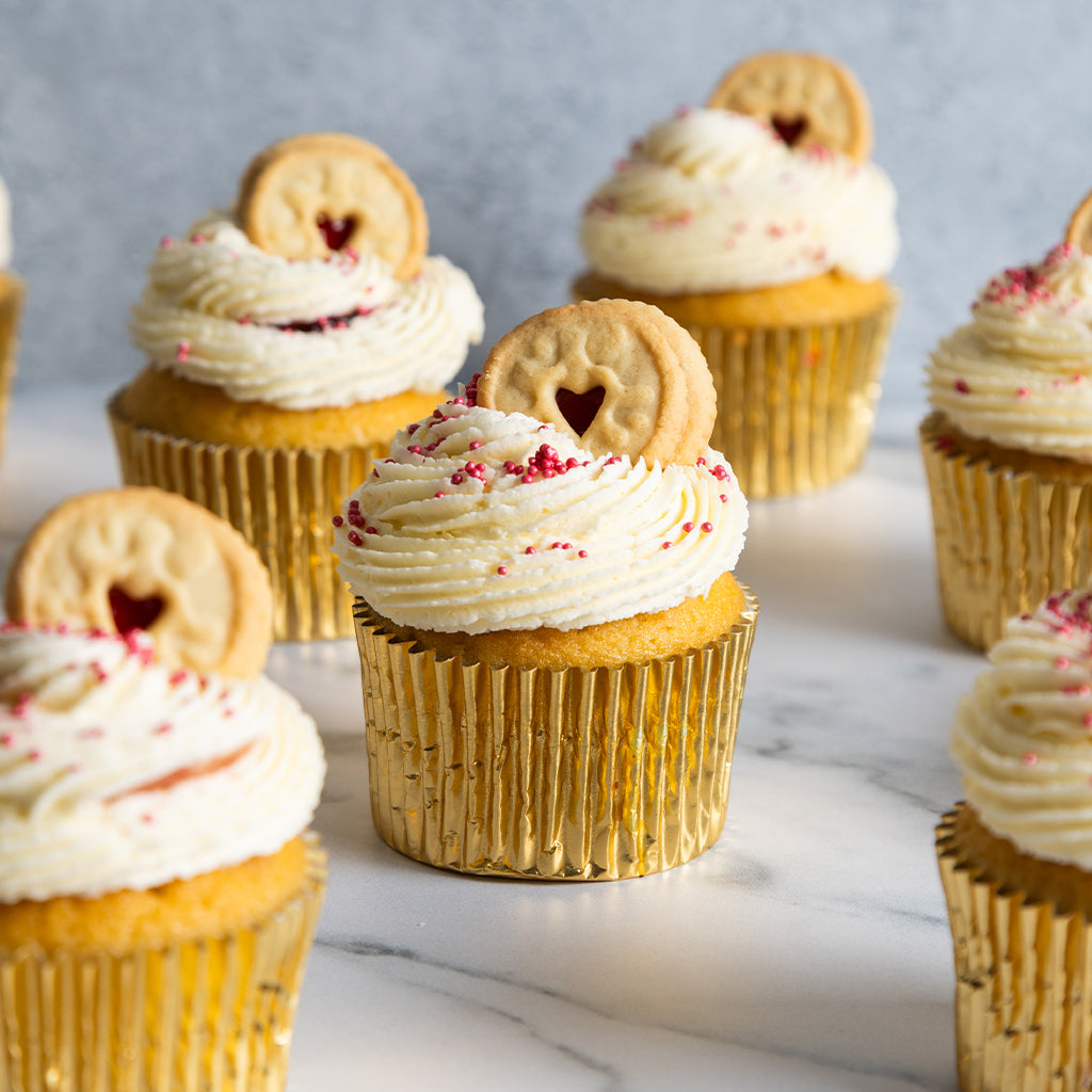 Cupcakes with white frosting and heart-shaped biscuits on a marble surface