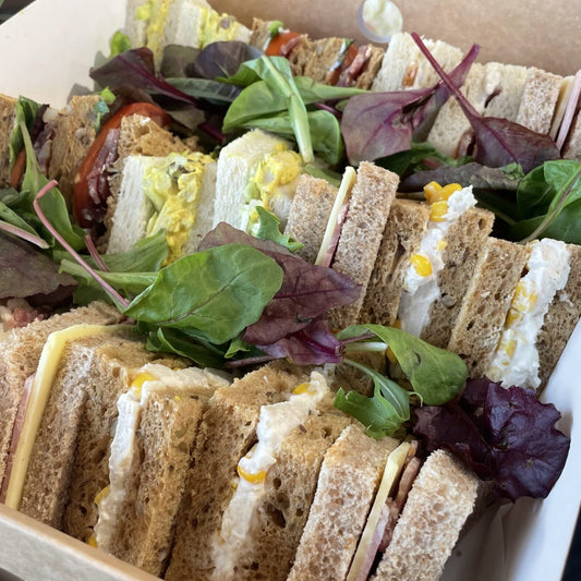 Assorted small meat filled sandwiches with different fillings on a bed of greens in a cardboard container.