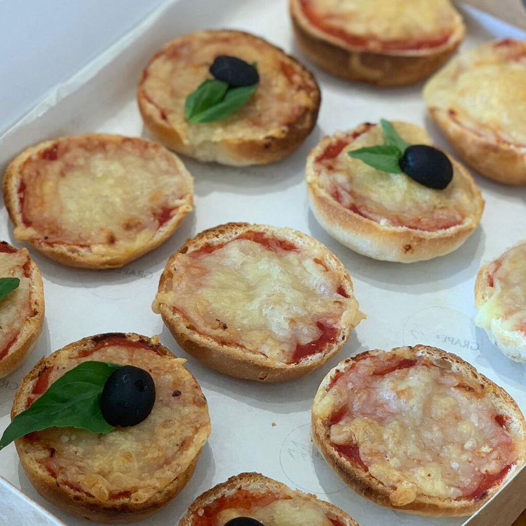 Mini pizzas with olives and basil leaves on a white surface