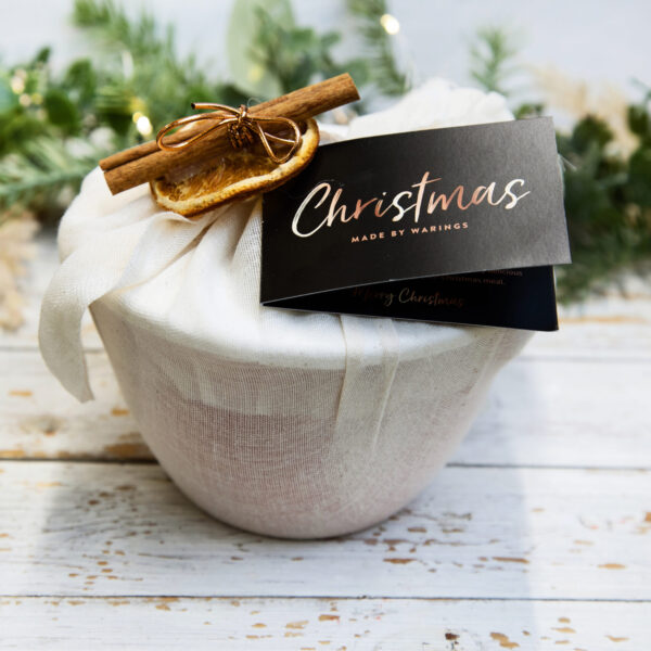 Christmas pudding in it's bowl, wrapped in muslin and tied with a cinamon stick and dried orange slice. Finished with product provenance tag