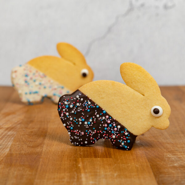 Two bunny shaped biscuits standing, staggered one behind the other. Picture set against a grey background on a wooden table.