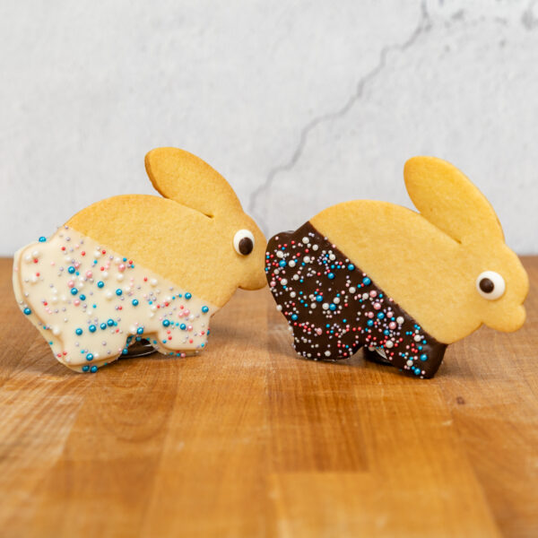 Two bunny shaped biscuits standing, following each other. Picture set against a grey background on a wooden table.