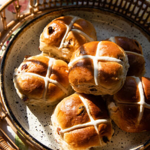 Six Hot Cross Buns displayed on a plate carried by a wicker tray