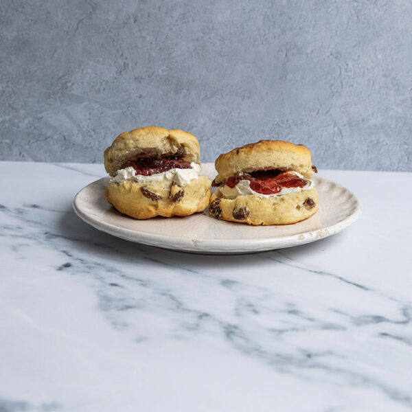 two scones filled with clotted cream and jam displayed on a plate against nuetral background